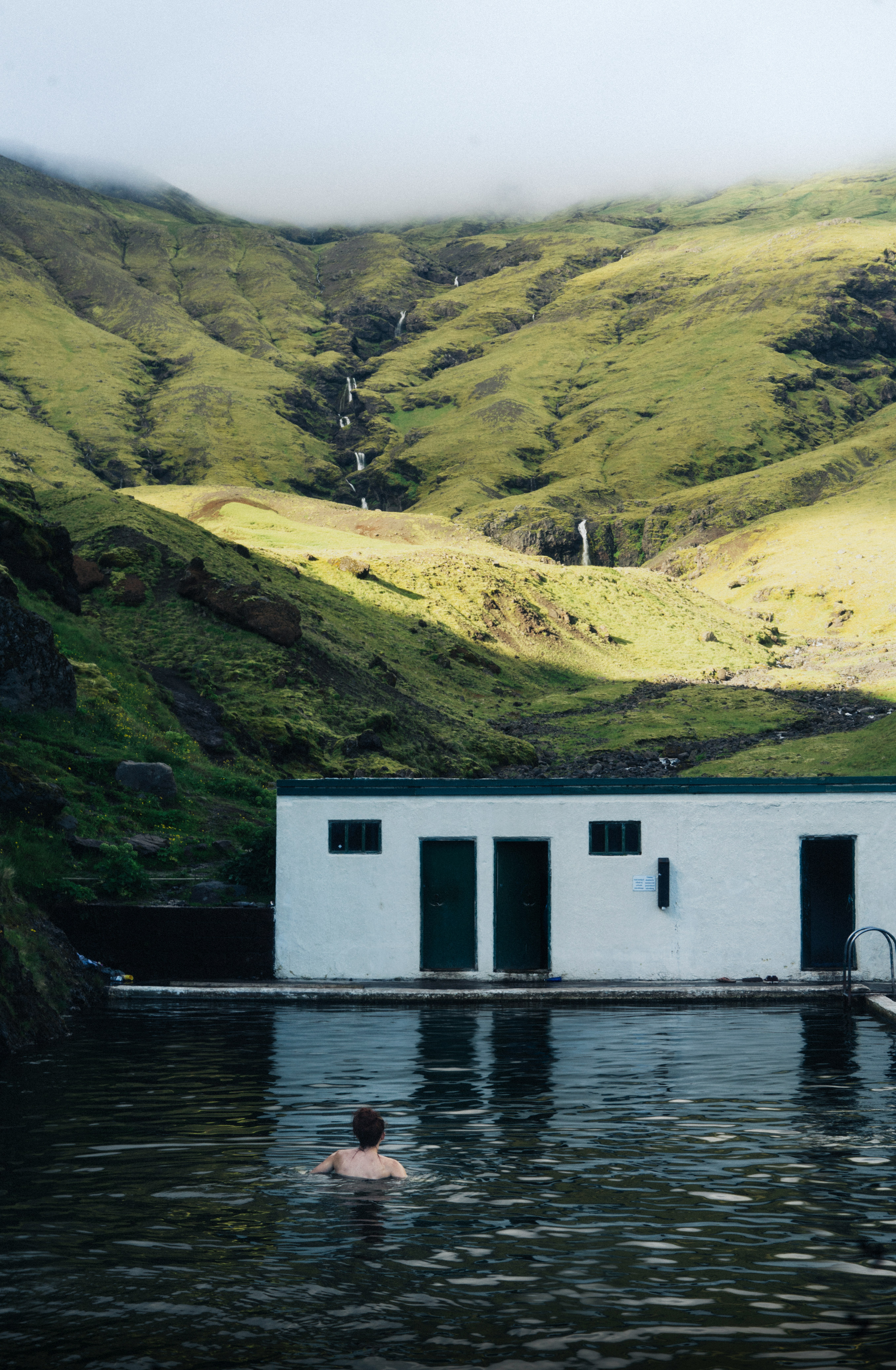 A solitary swimmer in a geothermal pool set into the hills of Iceland — a quiet morning, no one else around.